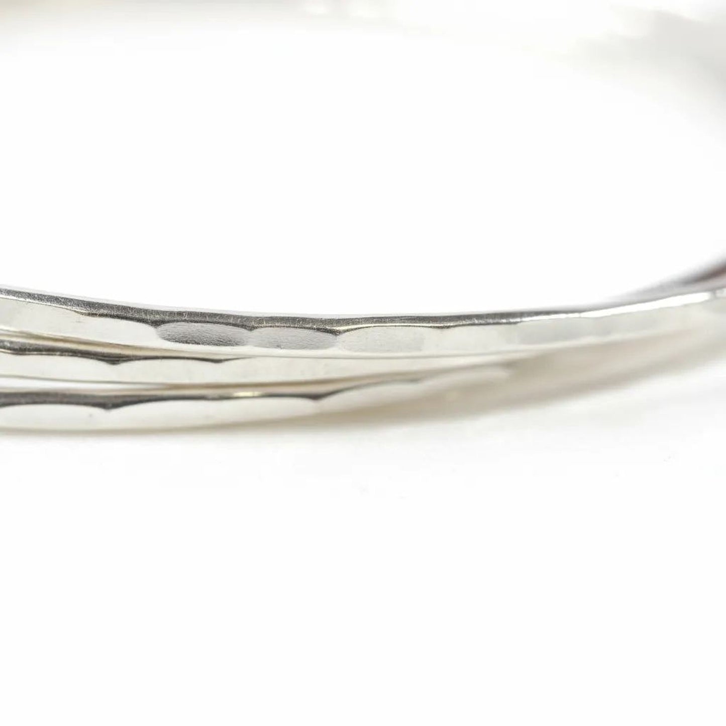 A close-up view of a silver bracelet with a textured surface, resting on a white background.
