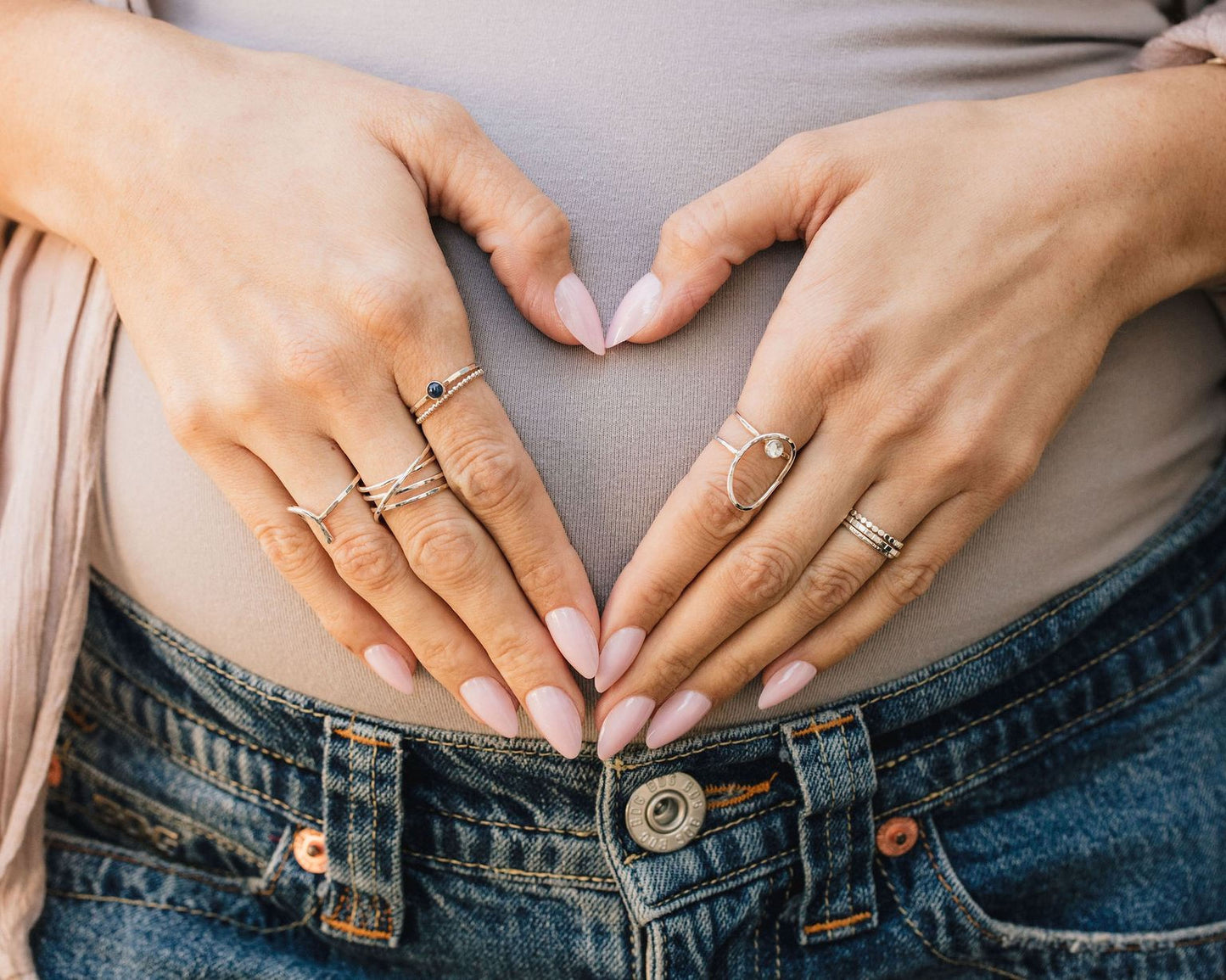 A close-up image of a person's hands forming a heart shape, with rings on the fingers and a ring on the thumb.