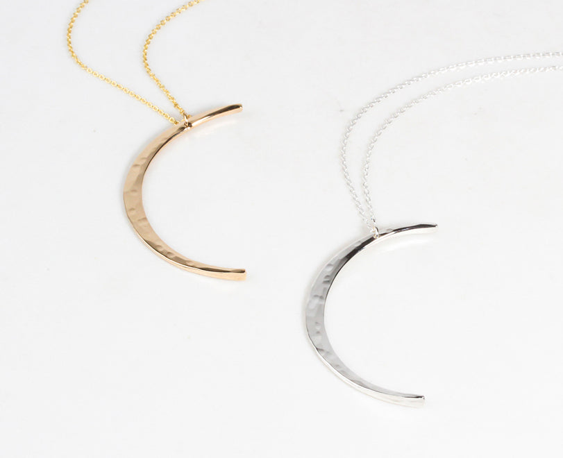 Image shows close up of both our sterling silver and 14 karat yellow gold filled moons. Delicately and intentional hand hammered to mimic the look of the moon, these handcrafted moons are made by our team of local artists. Moon measures 44mm long.