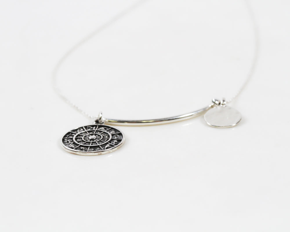 A brilliant zodiac sterling silver coin and textured disc hang spaced apart by a smooth tube bead and a rondelle bead. Handmade in house by our team of local artisans in the USA, this unique Kismet Celestial Necklace is sure to catch eyes.