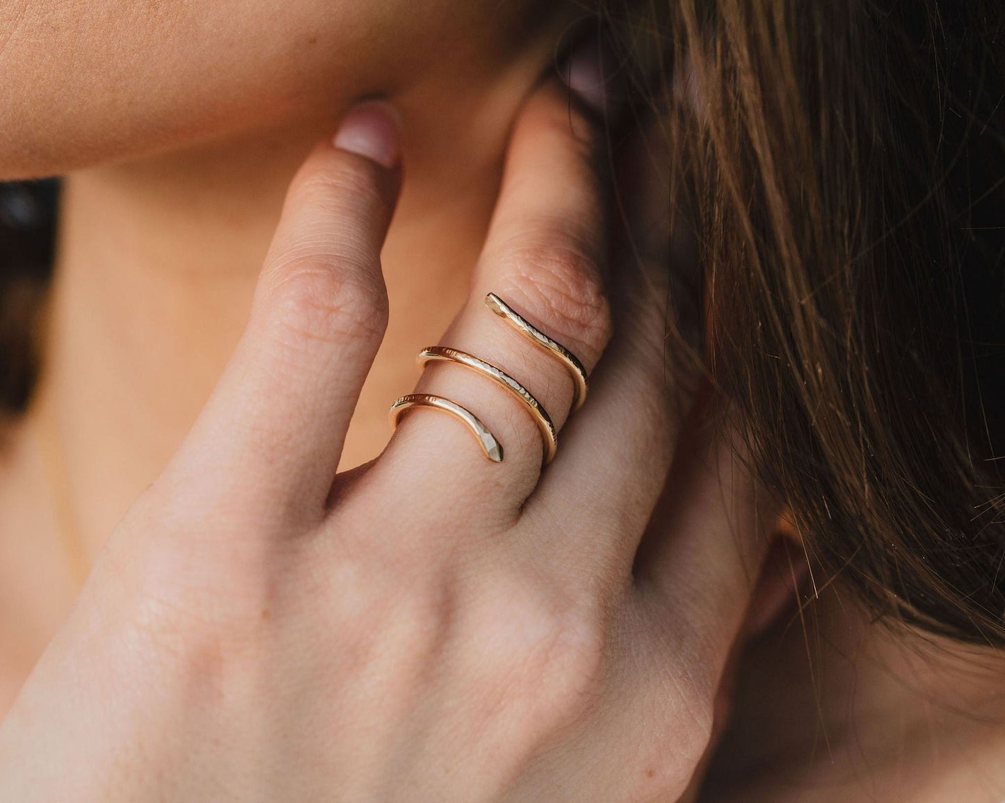 A close-up of a person's hand wearing a gold snake-shaped ring on the ring finger.