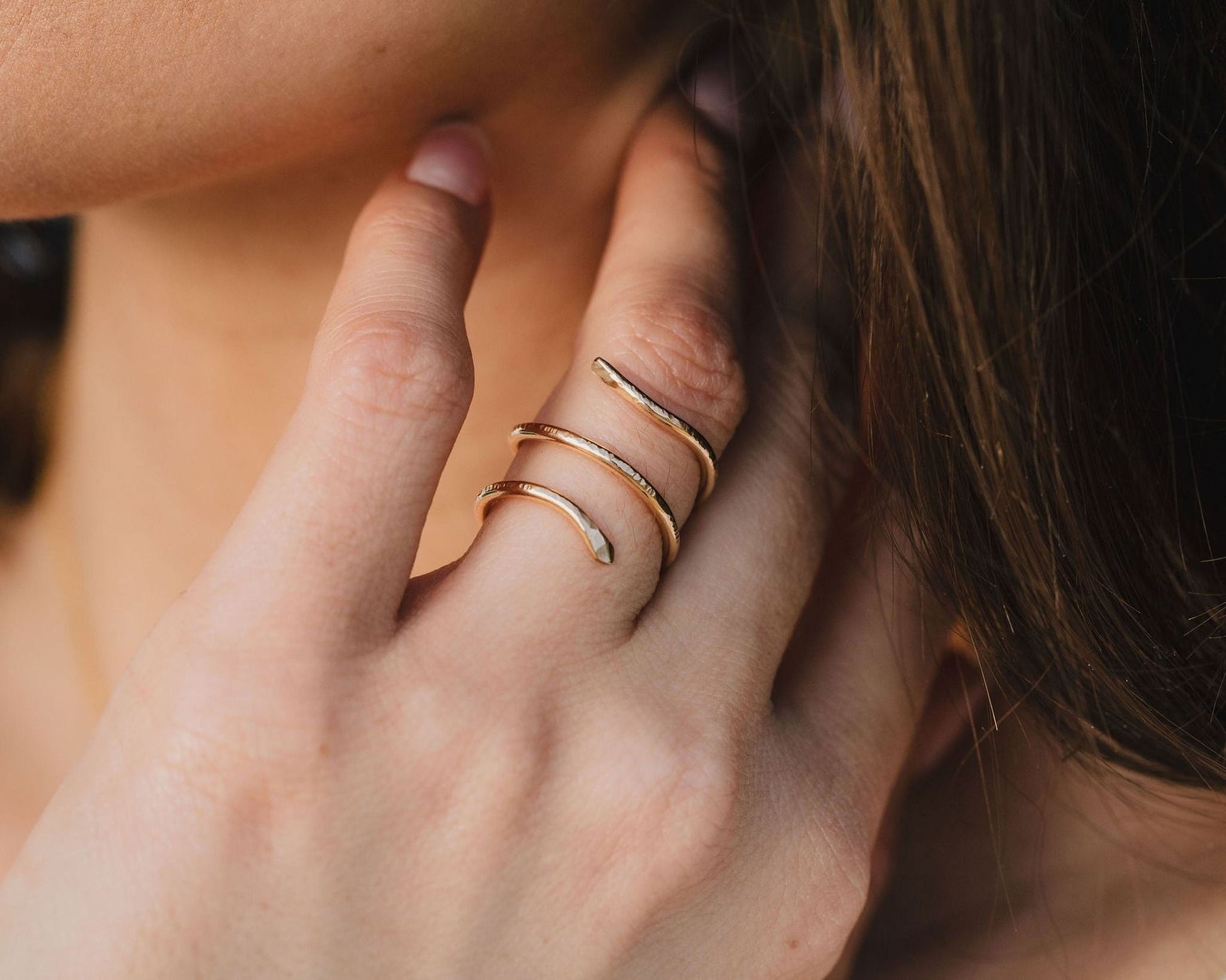 A close-up of a person's hand wearing a gold snake-shaped ring on the ring finger.