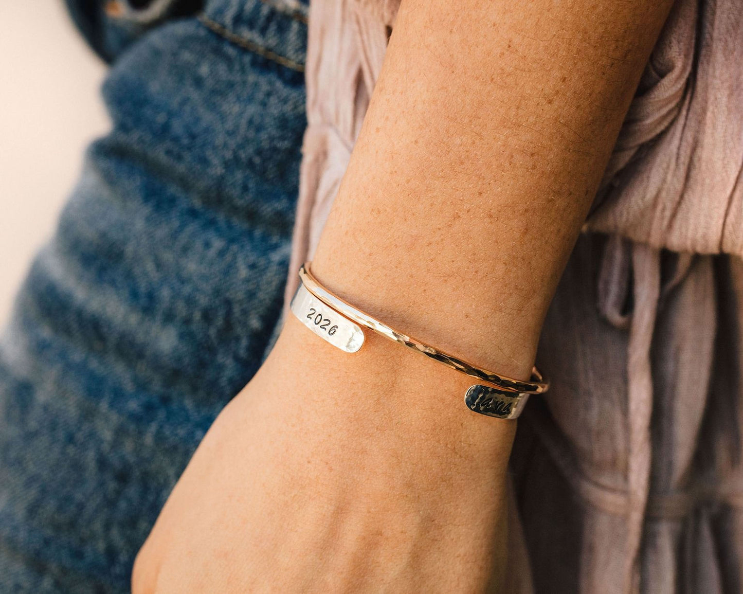 A gold bracelet with the year "2024" engraved on it, worn on a person's wrist.