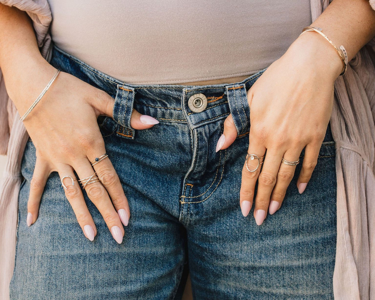 A close-up view of a person's hands wearing multiple rings on their fingers, with the focus on the fingers and the jeans below.