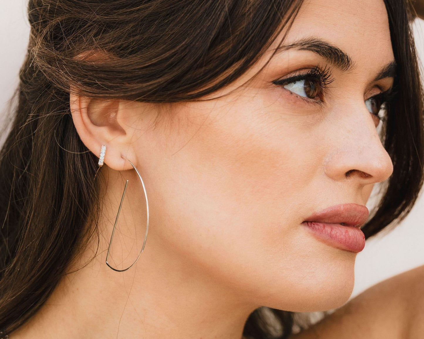 A close-up of a woman's face, with her eyes closed and her gaze directed to the side. She is wearing large hoop earrings that are silver in color.