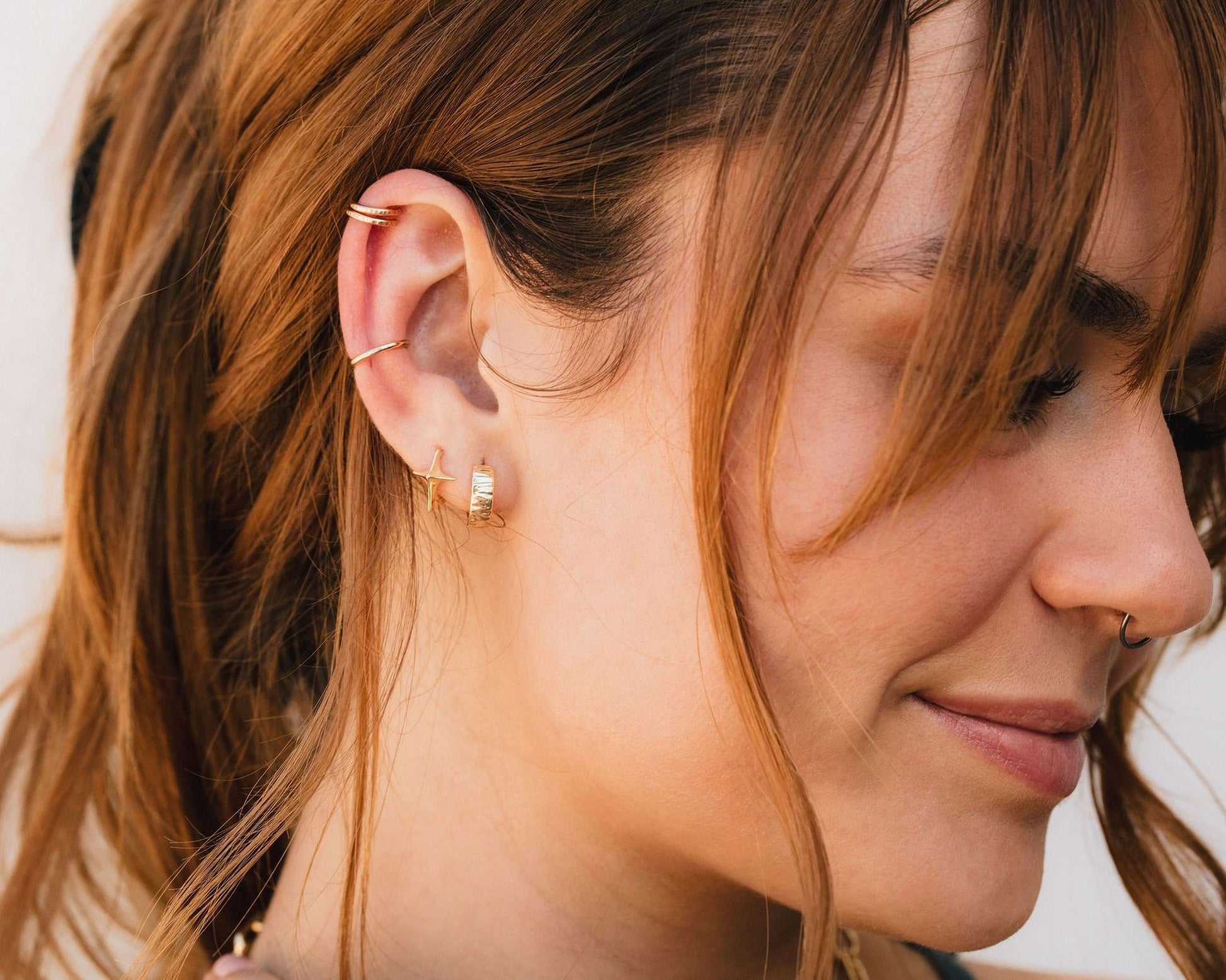 A close-up of a woman's face, with her hair styled in loose waves and adorned with multiple earrings and an earring in her left ear.