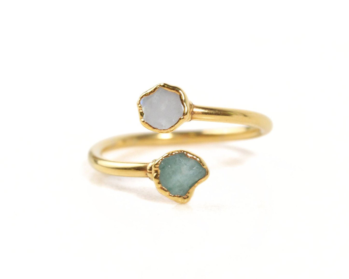 A gold ring with two gemstone stones, one white and one green, set in the center of the band.