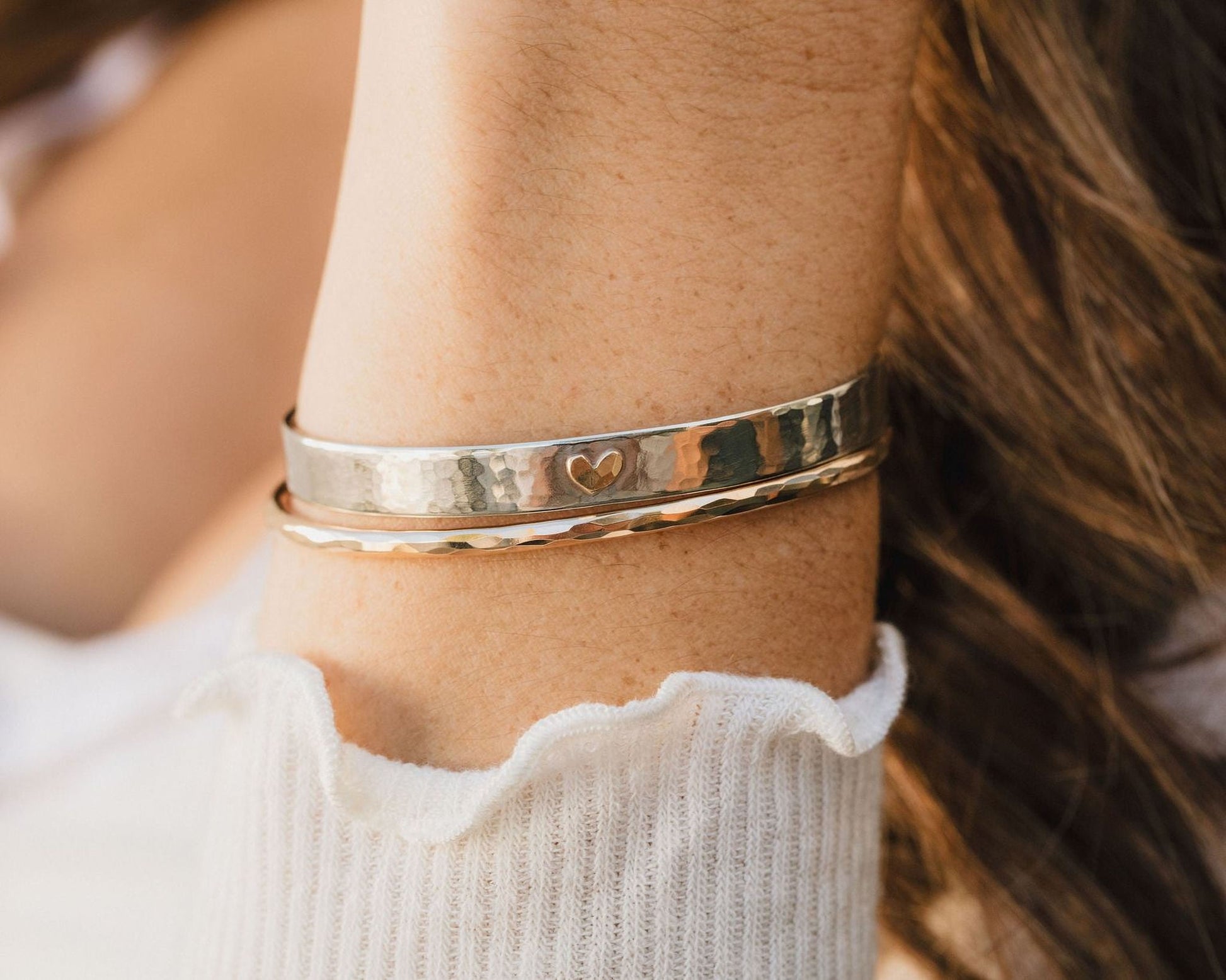 A close-up view of a person's arm wearing a silver bracelet with a heart-shaped charm.