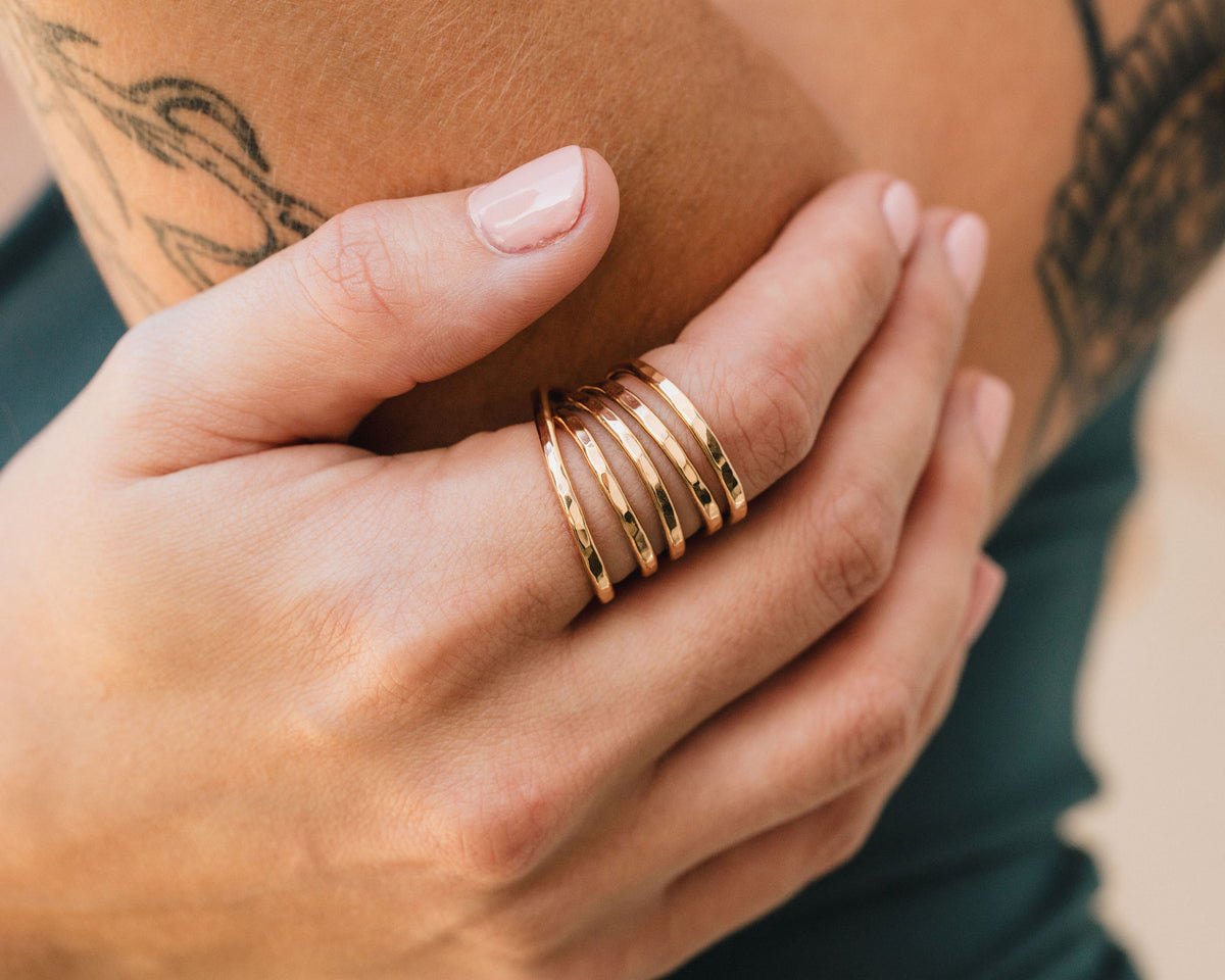 A close-up image of a person's hand wearing a gold ring with multiple bands, resting on a green surface.