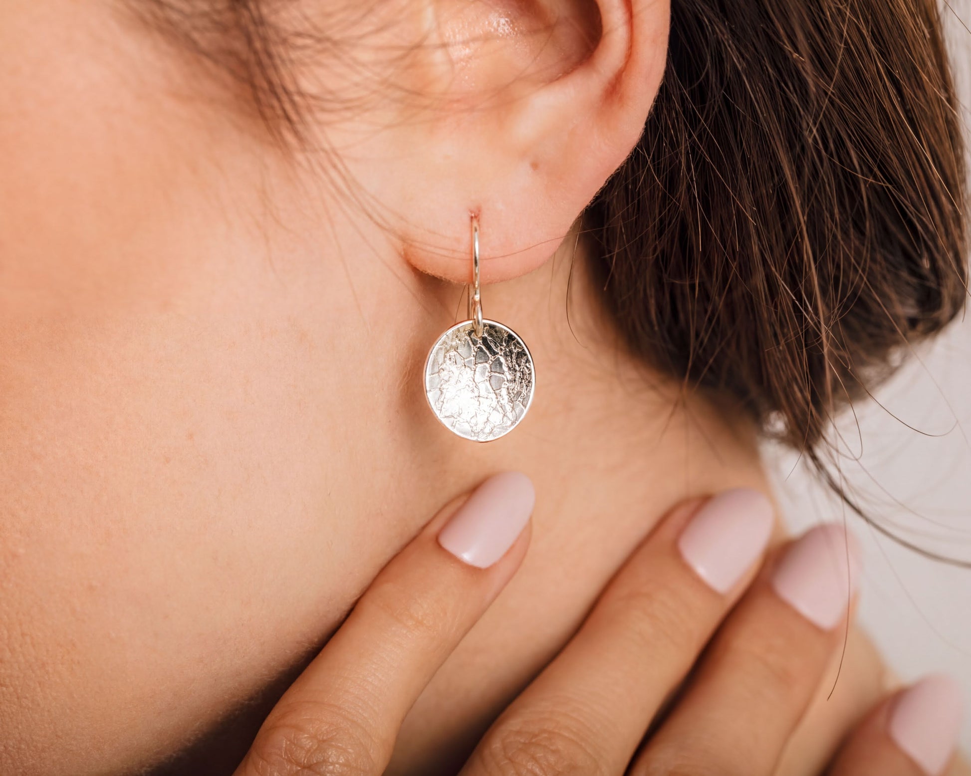 A close-up view of a woman's ear adorned with a silver earring featuring a circular design.