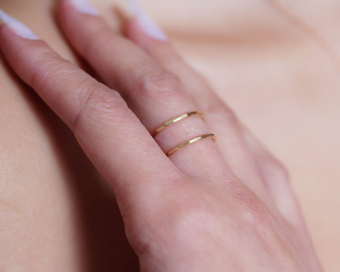 A close-up of a person's hand wearing two gold rings on the fingers.