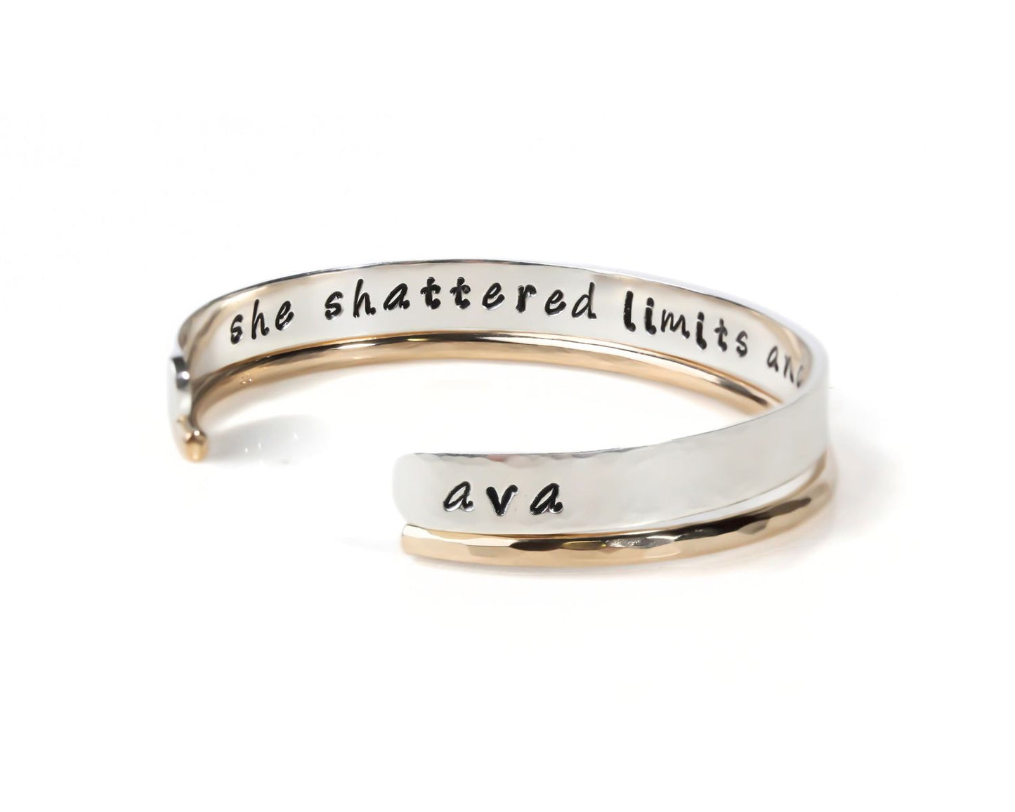 A silver and gold bracelet with the text "she shattered limits and ava" engraved on it.