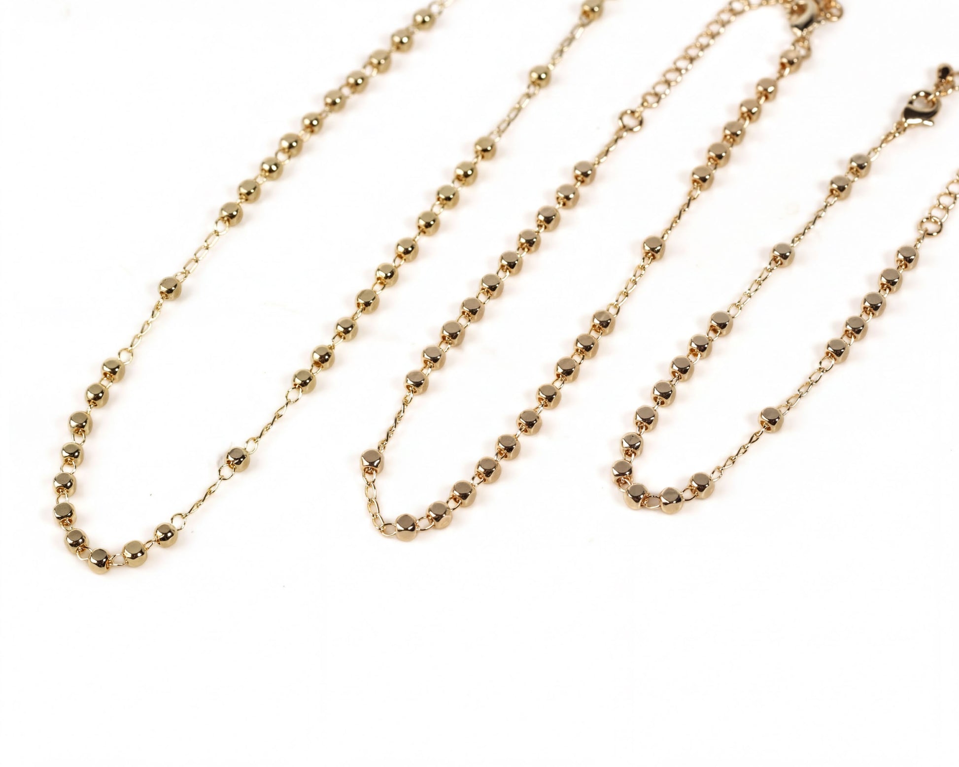 three gold-colored necklaces with small beads arranged in a row.