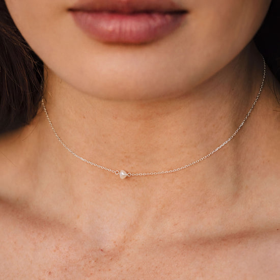A close-up of a woman's neck and chest area, featuring a delicate silver necklace with a small pendant.