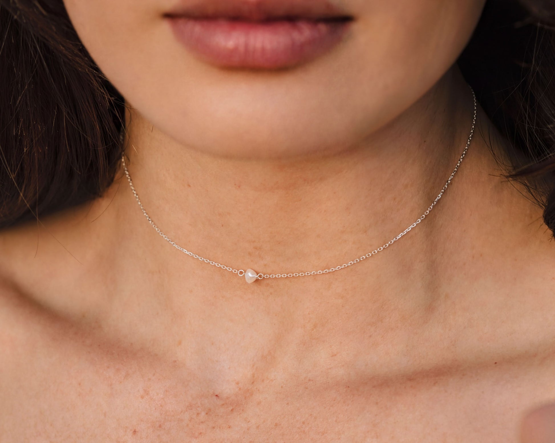 A close-up of a woman's neck and chest area, featuring a delicate silver necklace with a small pendant.