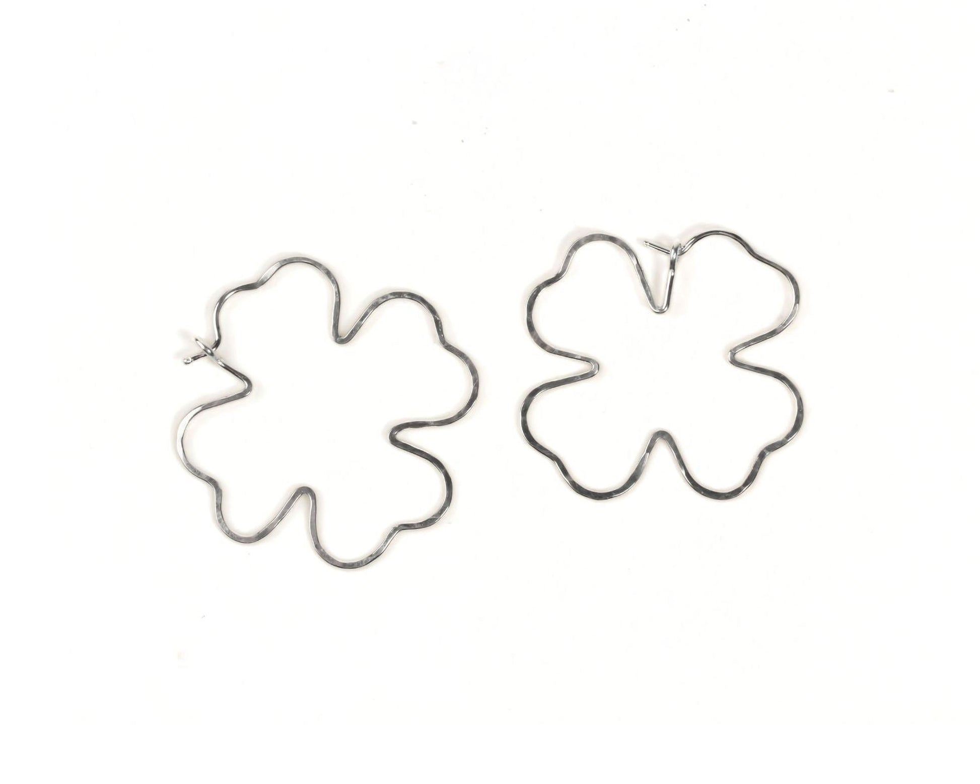 two silver earrings in the shape of leaves, specifically clover-shaped leaves, against a white background.