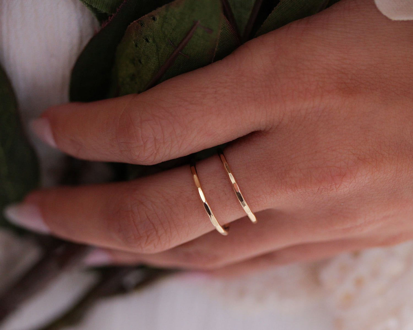 A close-up view of a person's hand wearing a gold ring with two bands, resting on a green leaf.