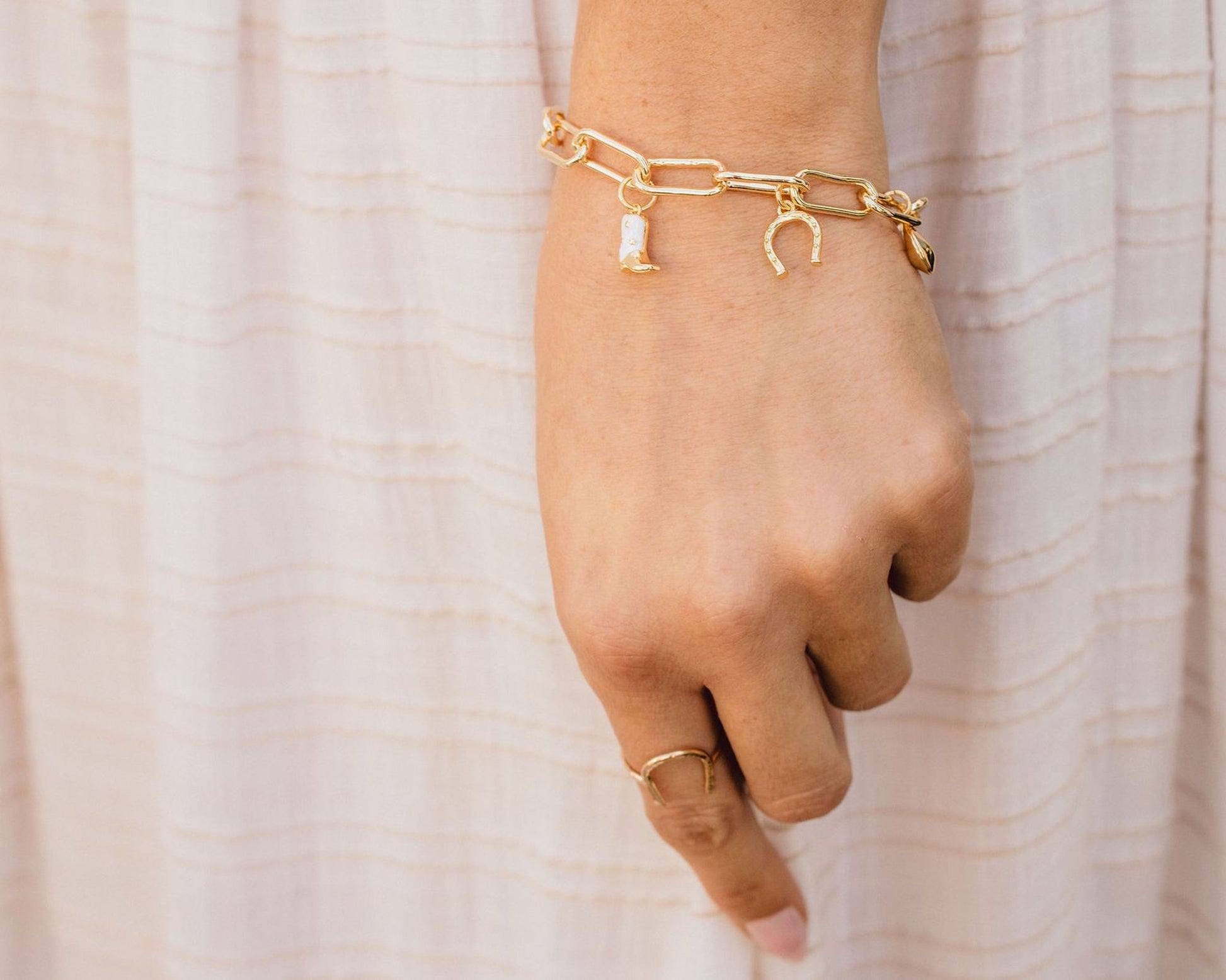 A close-up view of a person's hand wearing a gold bracelet and ring against a white background.