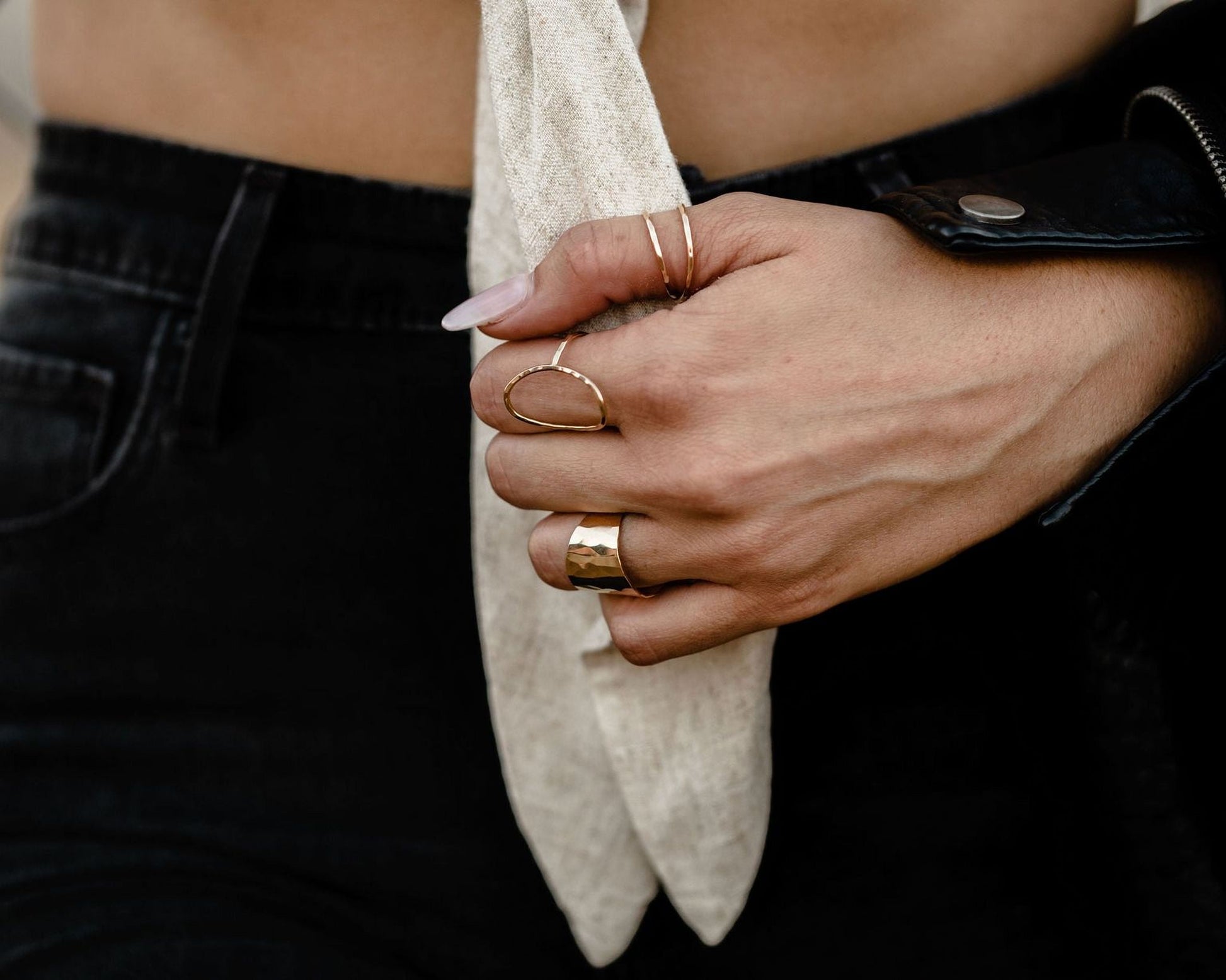 A close-up of a person's hand wearing multiple rings, including a gold ring on the ring finger and other rings on the other fingers.
