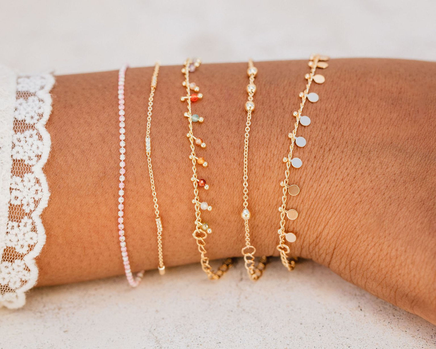 A close-up view of a person's wrist adorned with multiple gold-colored bracelets of various designs and lengths.