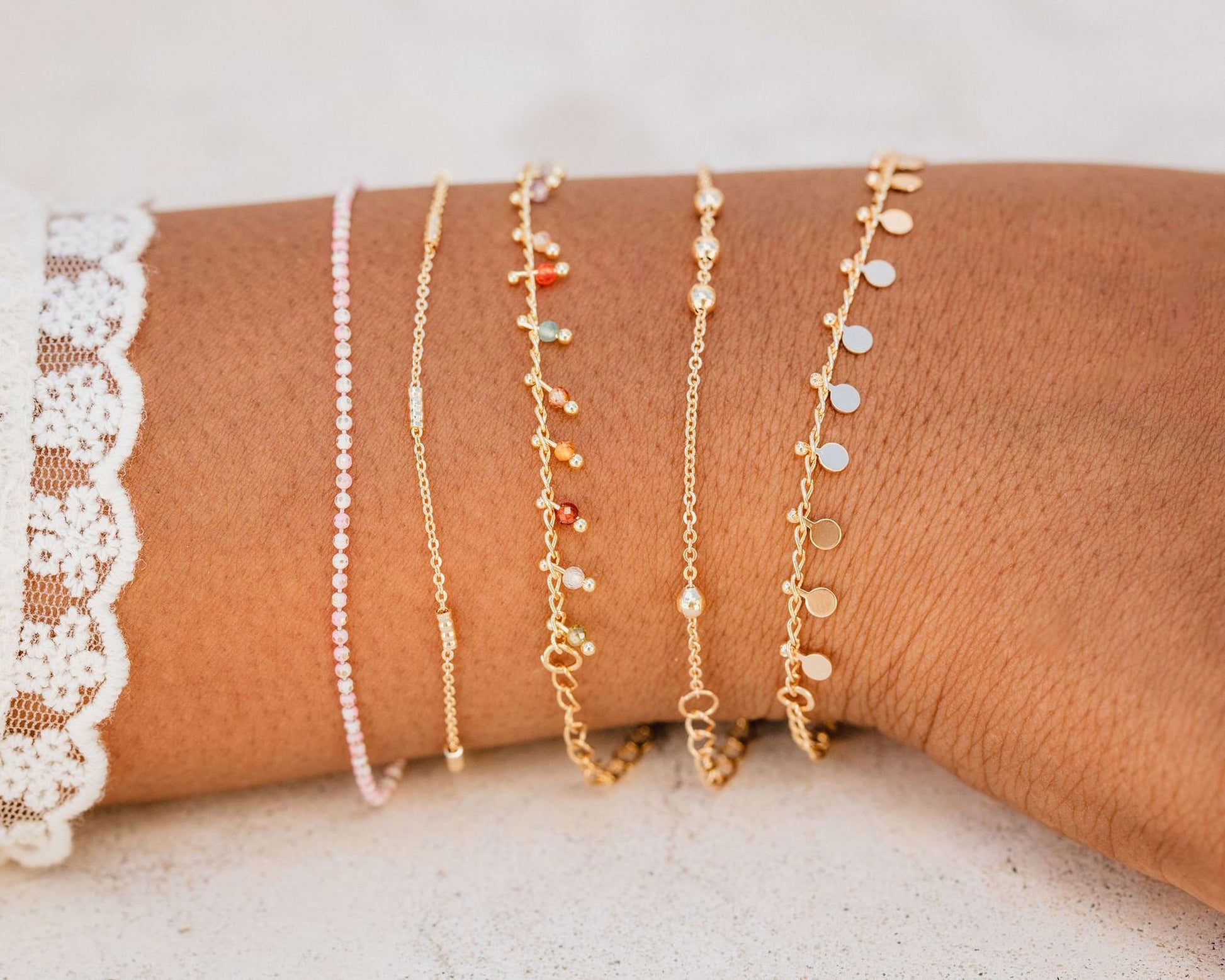 A close-up view of a person's wrist adorned with multiple gold-colored bracelets of various designs and lengths.
