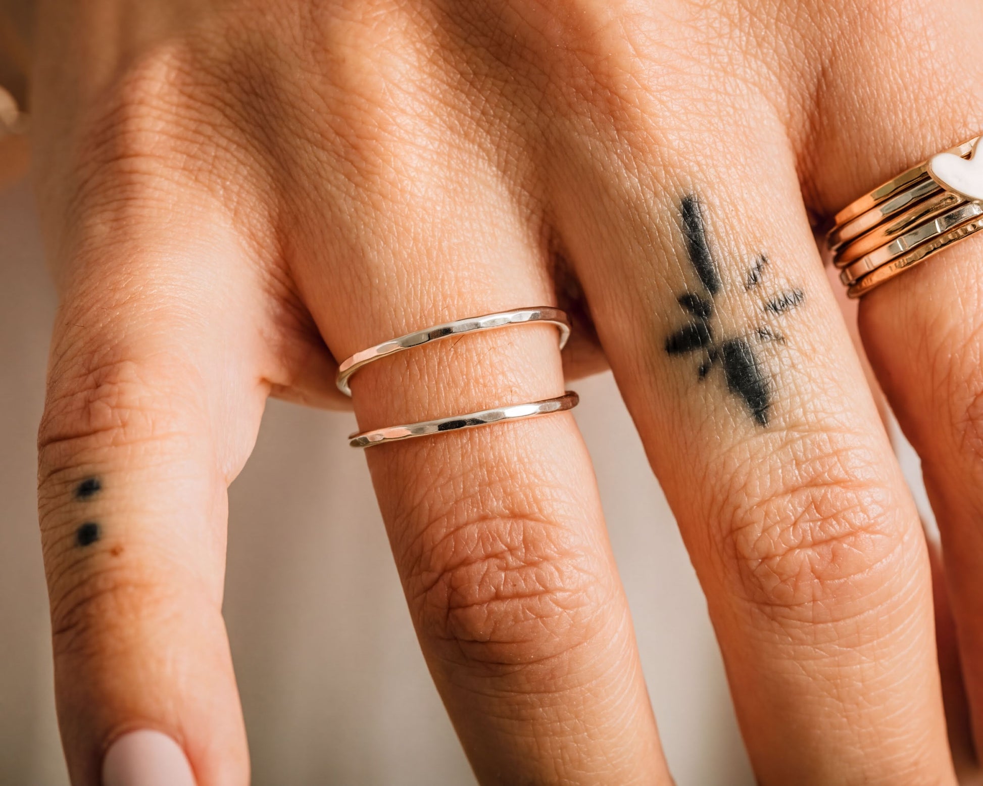 A close-up view of a person's hand adorned with multiple rings and a tattoo on the finger.