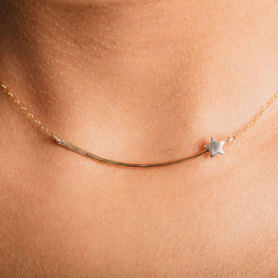 A delicate gold necklace with a small star charm is shown in close-up, highlighting the intricate details of the piece.