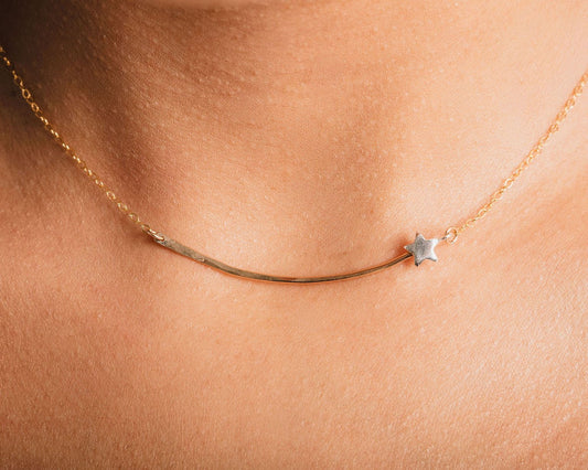 A delicate gold necklace with a small star charm is shown in close-up, highlighting the intricate details of the piece.