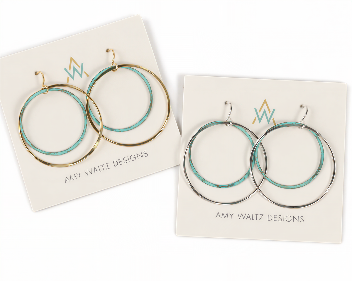 a pair of earrings with turquoise and gold tones, presented on white packaging with the brand name "AMY WAITZ DESIGNS" printed on them.