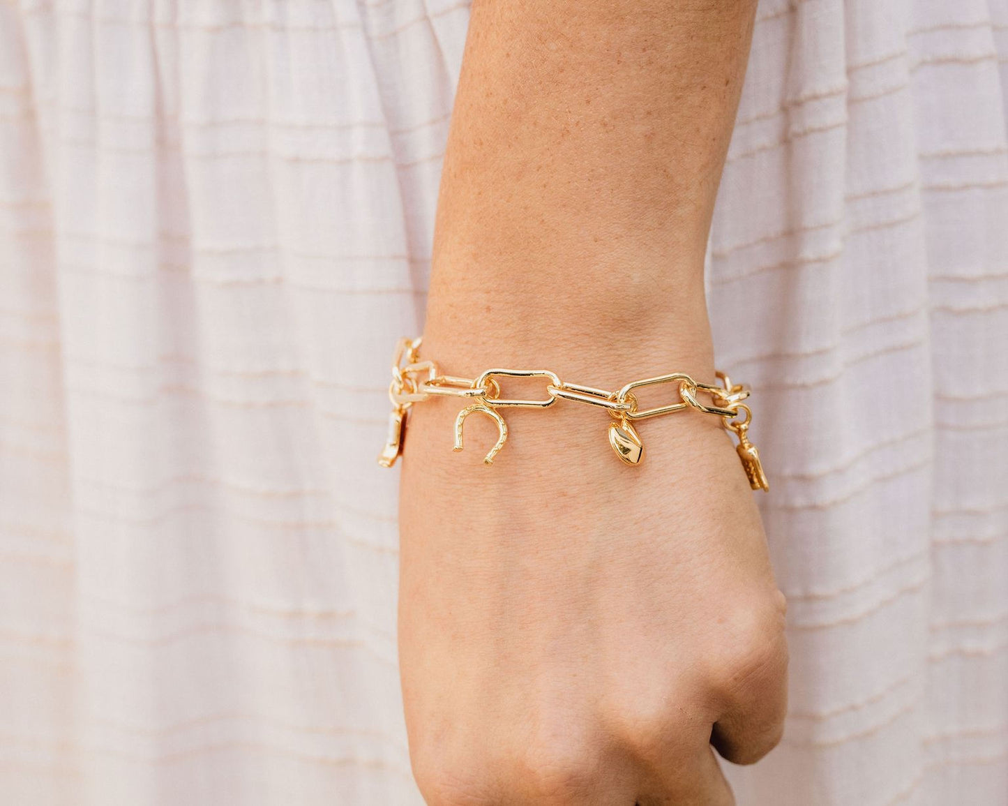 A close-up view of a person's wrist wearing a gold-colored bracelet with charms on it.
