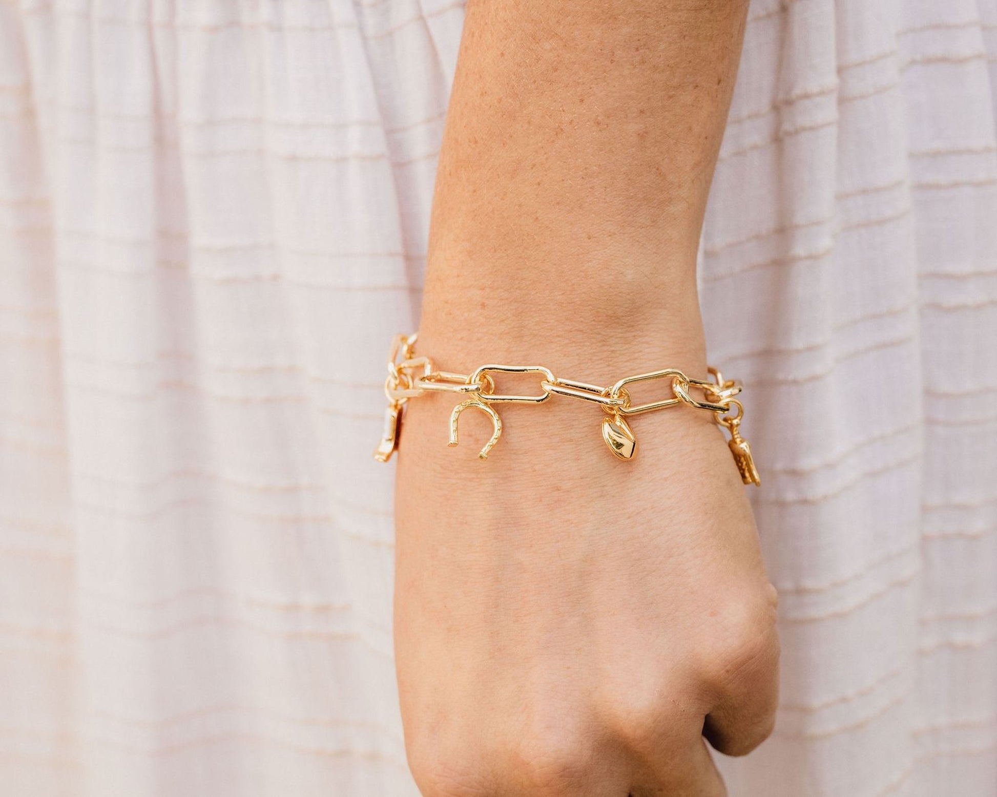 A close-up view of a person's wrist wearing a gold-colored bracelet with charms on it.