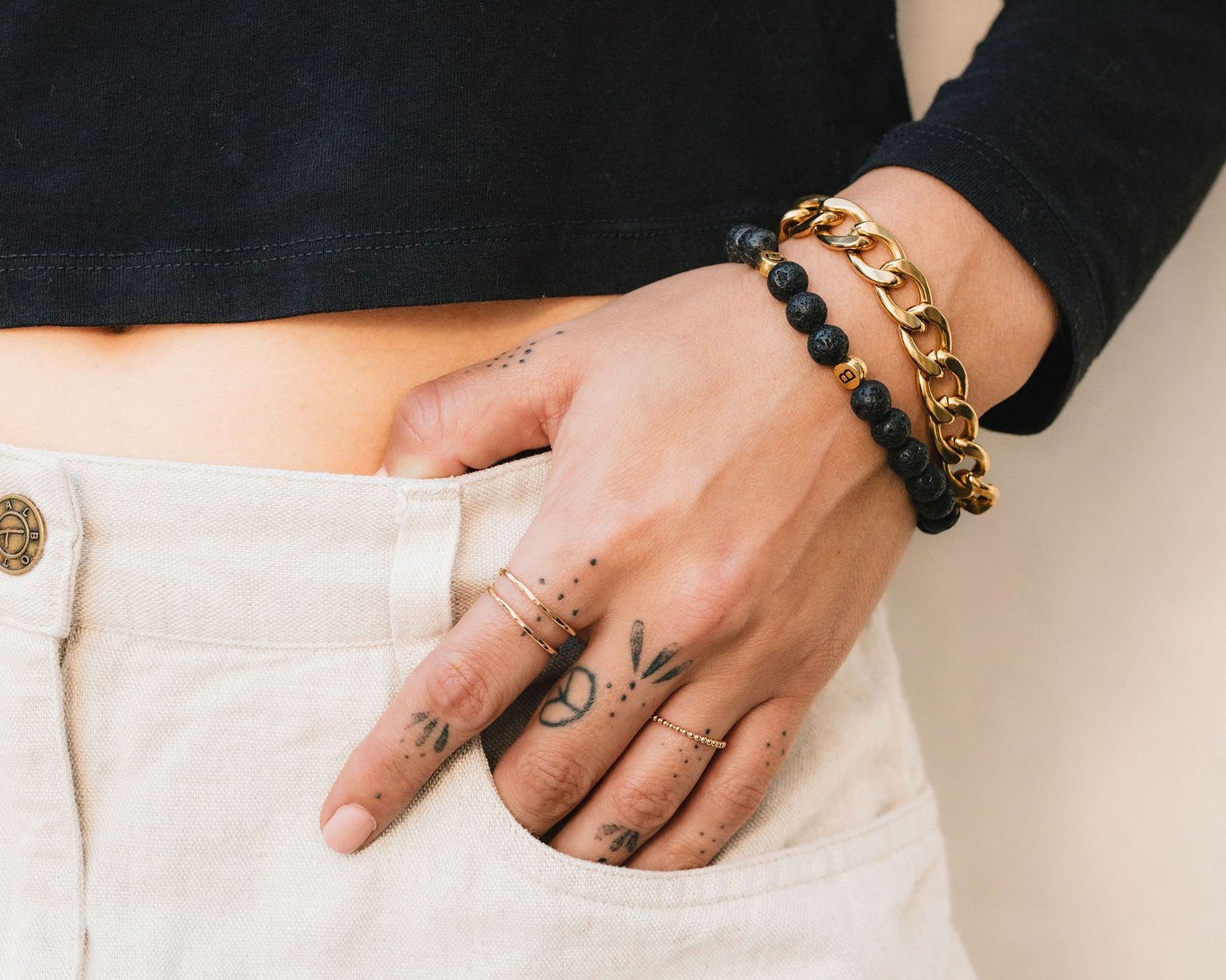 A person's hand wearing multiple rings and bracelets, with tattoos visible on the fingers.