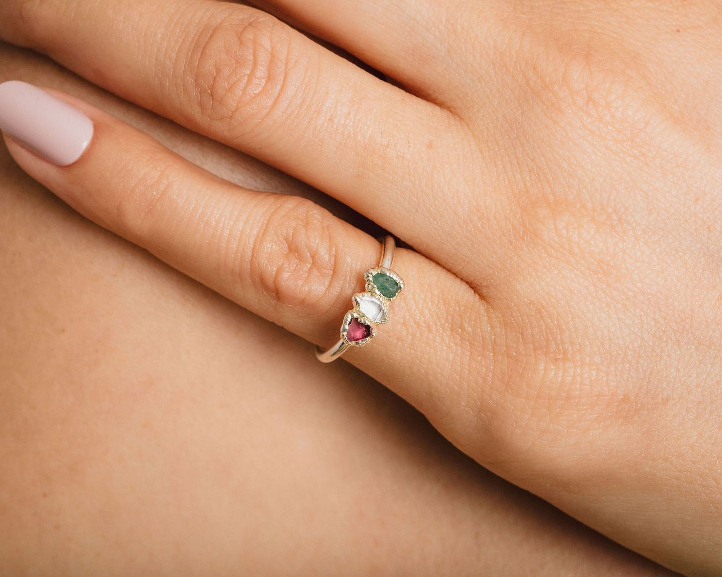 A close-up of a person's hand wearing a ring with three gemstones.