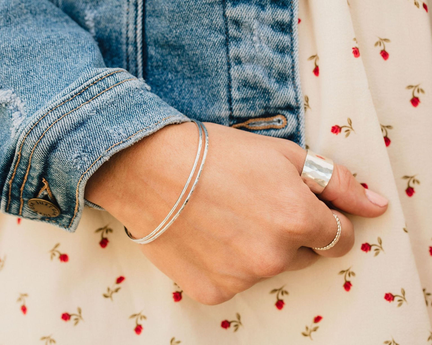 A close-up view of a person's hand wearing a bracelet and rings, with a denim jacket visible in the background.