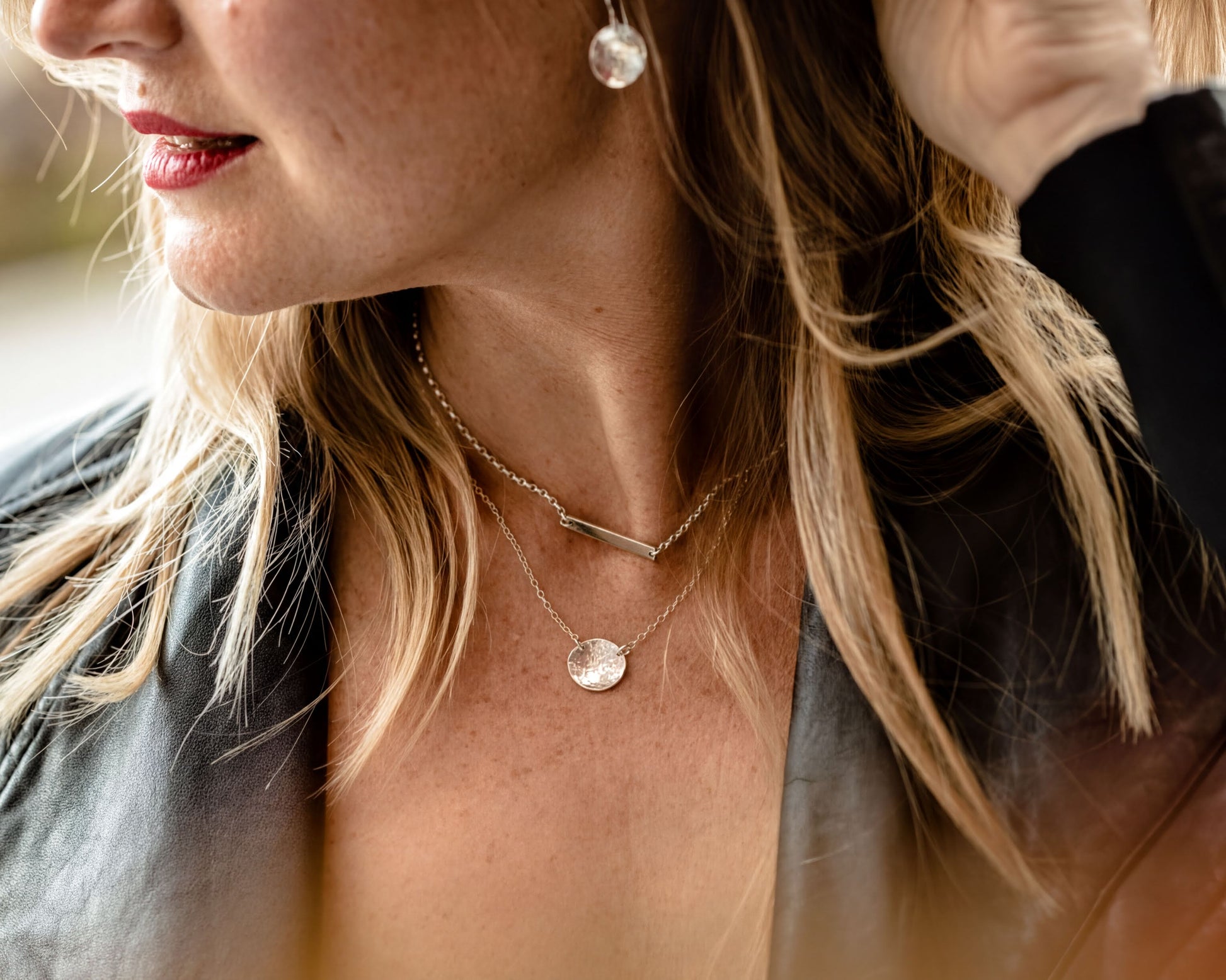 A close-up of a woman's neck and chest area, featuring a necklace with a pendant and earrings.