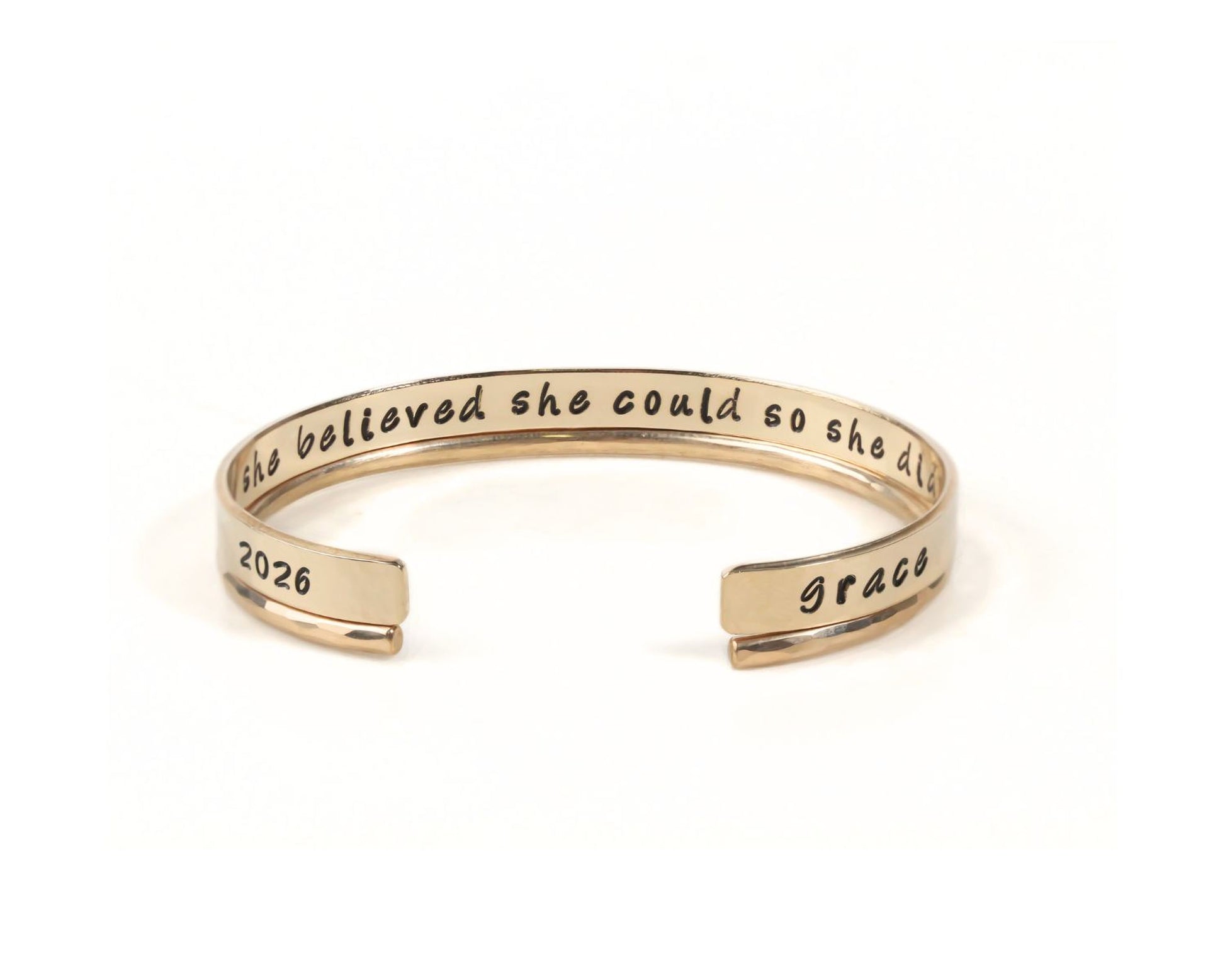 A gold-colored bracelet with a message engraved on it.