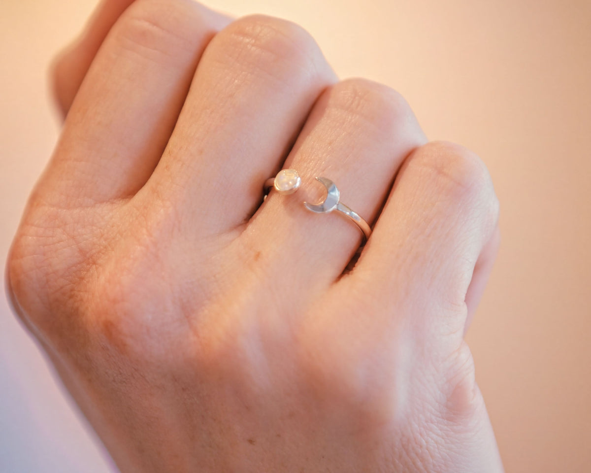 A close-up of a person's hand wearing a silver ring with a moon-shaped gemstone.