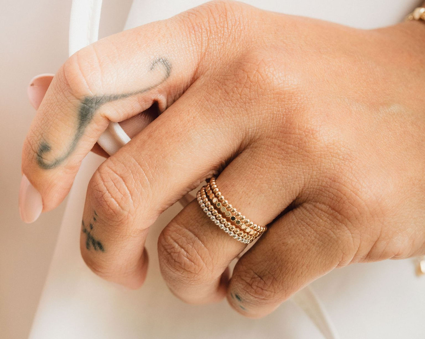 A close-up of a person's hand wearing a gold ring with multiple tiers and a tattoo on the left hand.