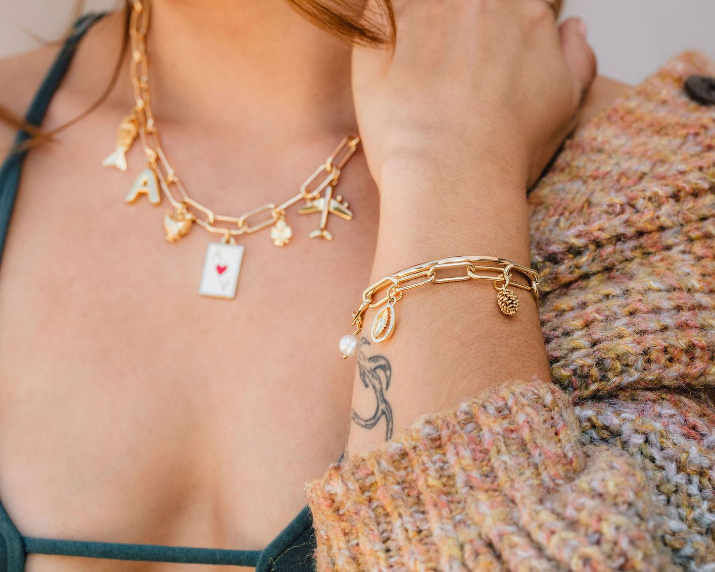 A close-up of a person's arm wearing a gold chain necklace and bracelet, with a tattoo visible on their wrist.