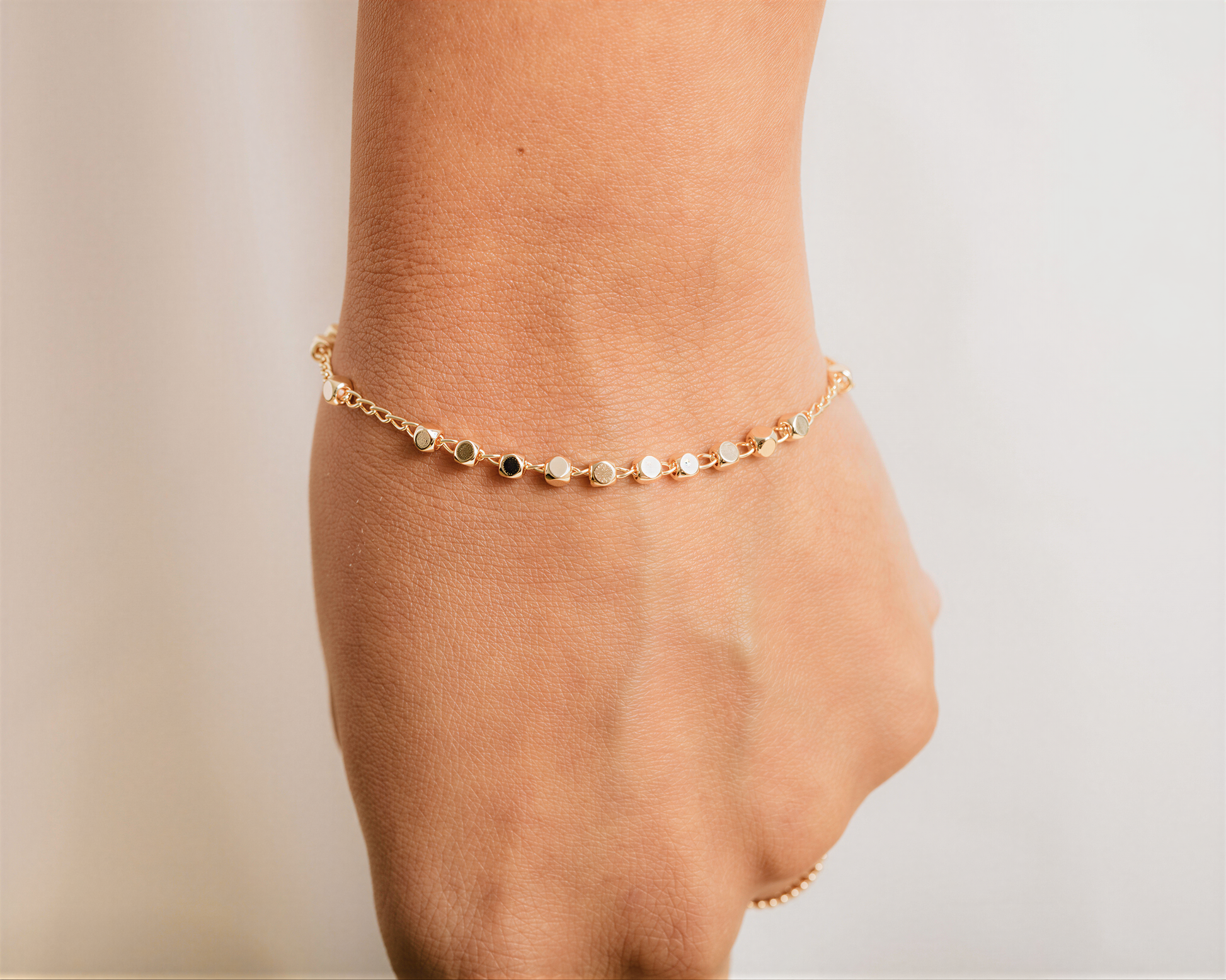 A close-up view of a person's wrist wearing a gold-colored bracelet with small circular charms.