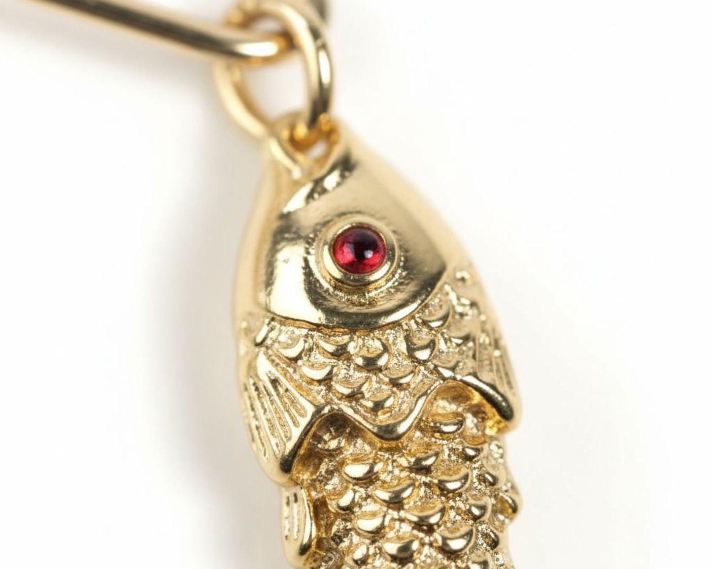 A close-up image of a gold-colored fish pendant with a red gemstone in the center.
