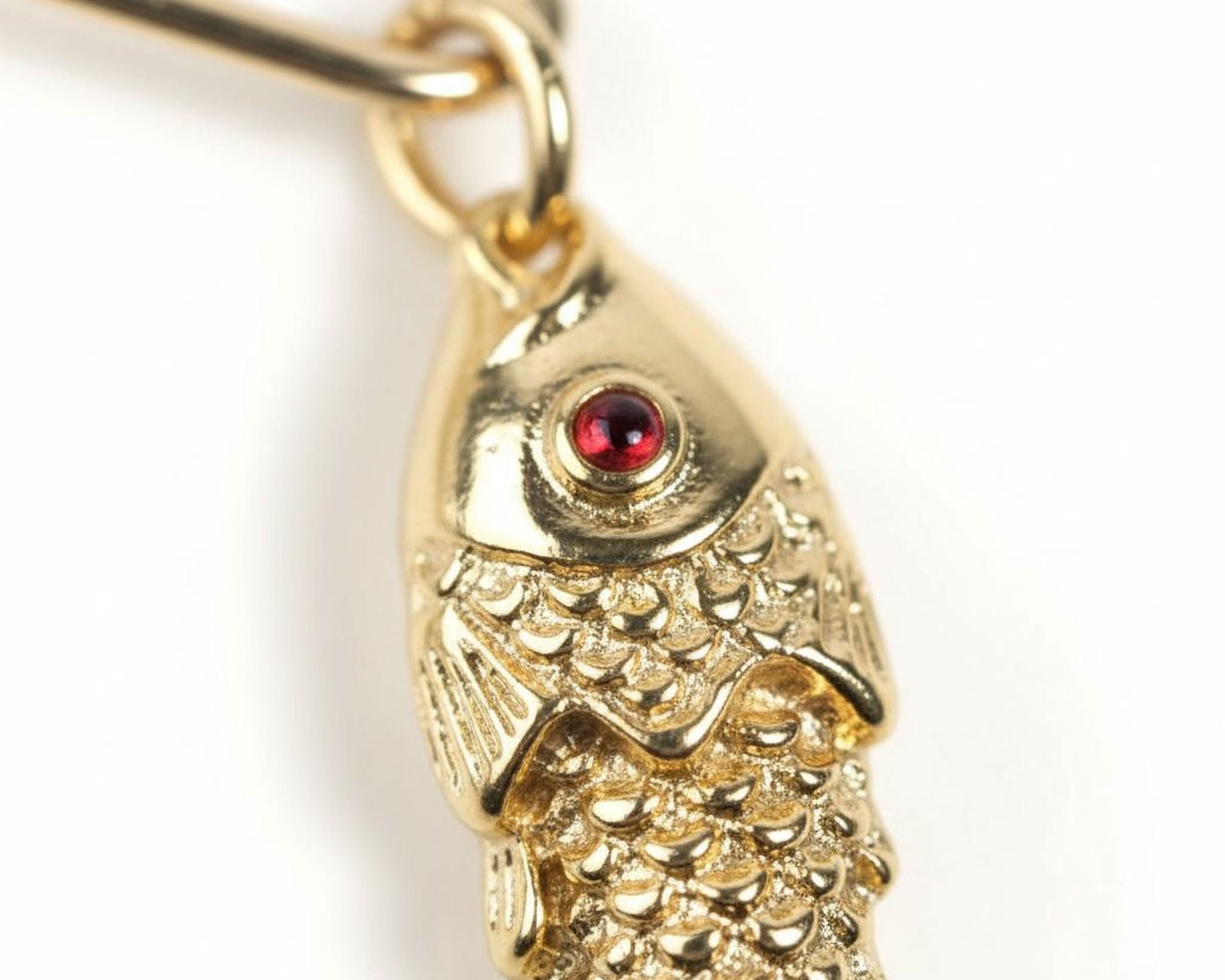 A close-up image of a gold-colored fish pendant with a red gemstone in the center.