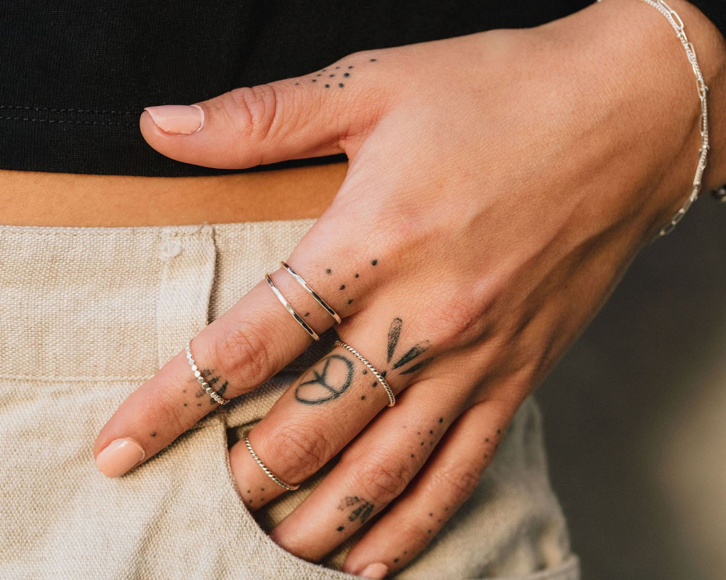 A close-up of a person's hand with multiple rings and tattoos on the fingers.