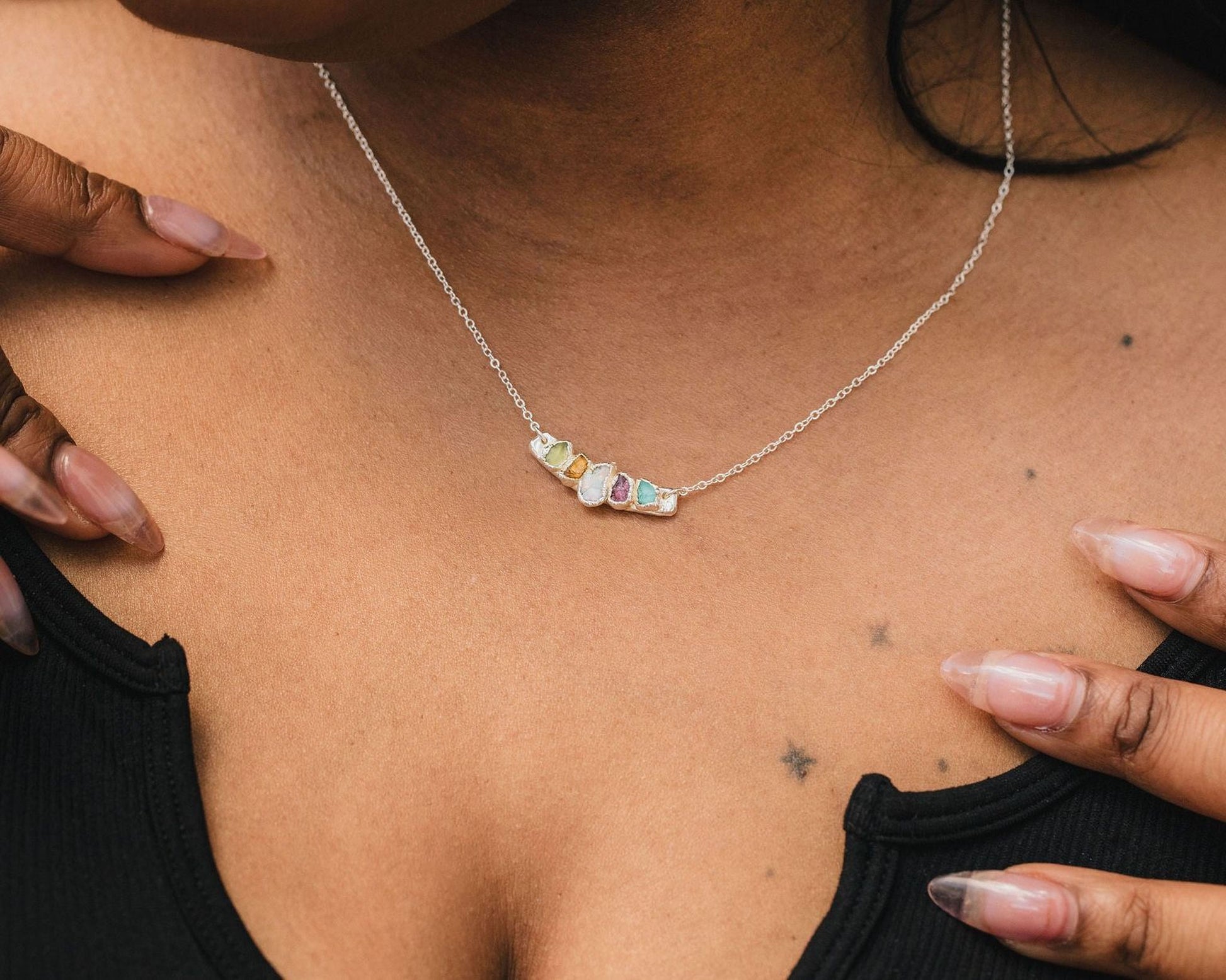 A close-up of a person's neck and chest area, with a silver necklace featuring colorful gemstones.