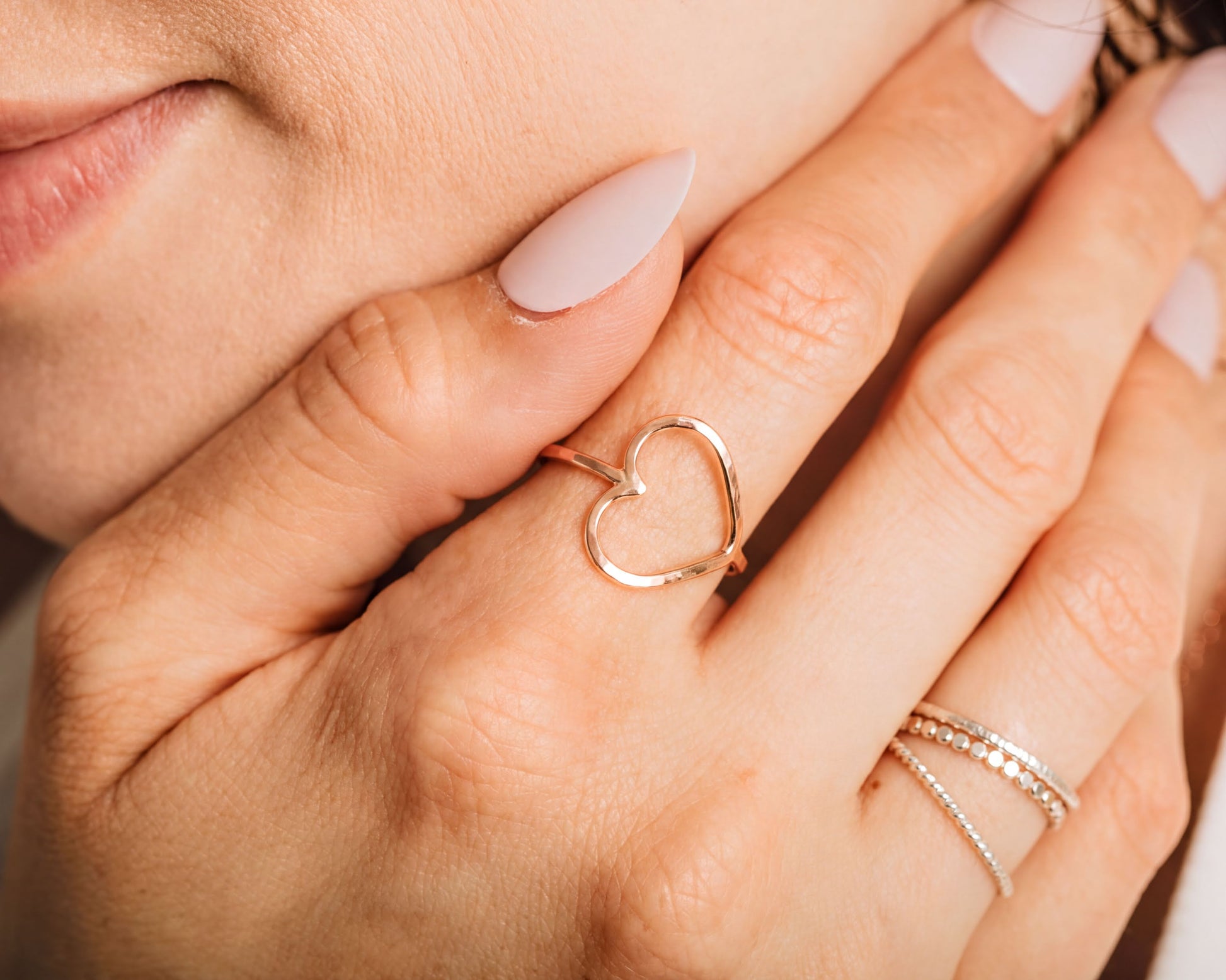 A close-up of a person's hand wearing a gold heart-shaped ring, with another ring visible on the same hand.