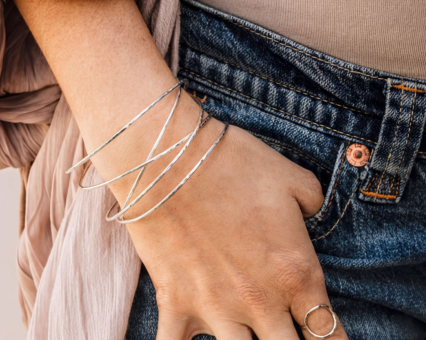 A close-up view of a person's hand wearing multiple silver bracelets on their wrist, with a denim skirt visible in the background.