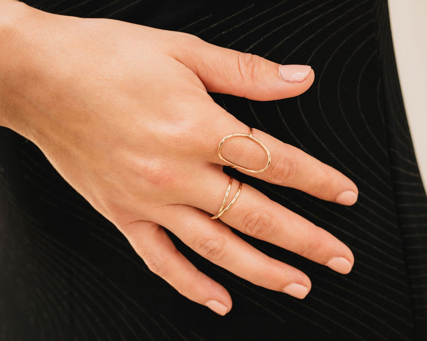 A close-up view of a person's hand wearing multiple rings, including a ring with a unique oval shape and another ring with a twisted design.