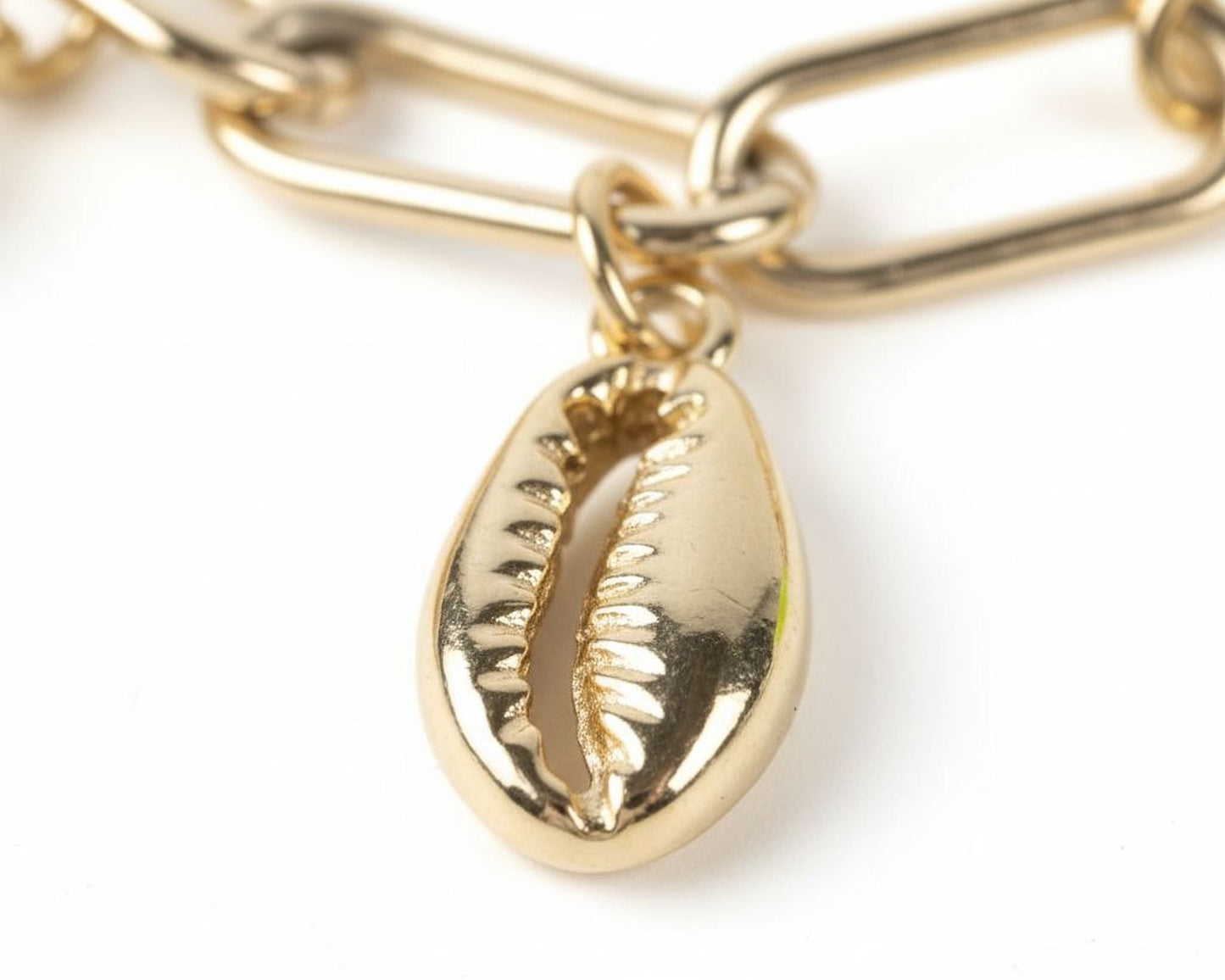 A close-up view of a gold-colored chain with a small, intricately designed shell pendant hanging from it.