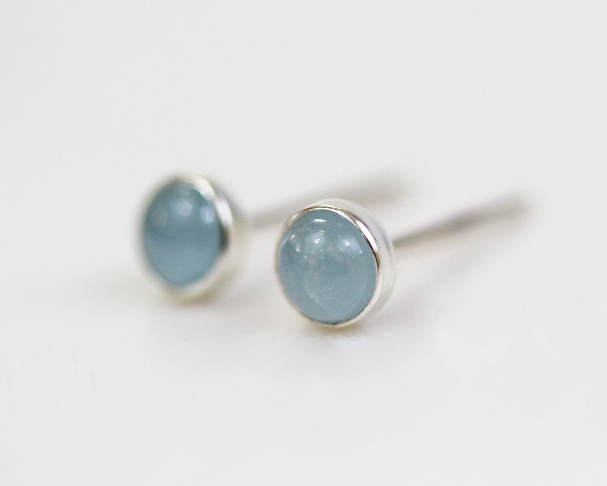 A pair of silver earrings with blue gemstones, resting on a white surface.