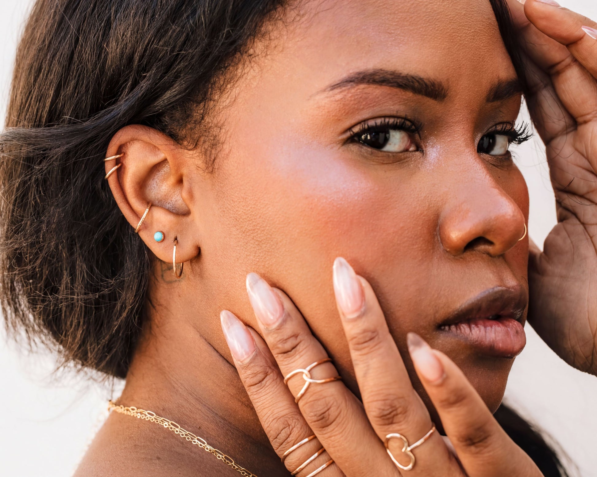 A close-up portrait of a woman with dark hair, wearing multiple rings on her fingers and earrings.